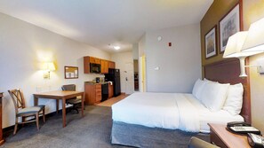 Ein Hotelzimmer mit Bett, Schreibtisch, Stuhl, Küchenzeile und Telefon auf dem Nachttisch.