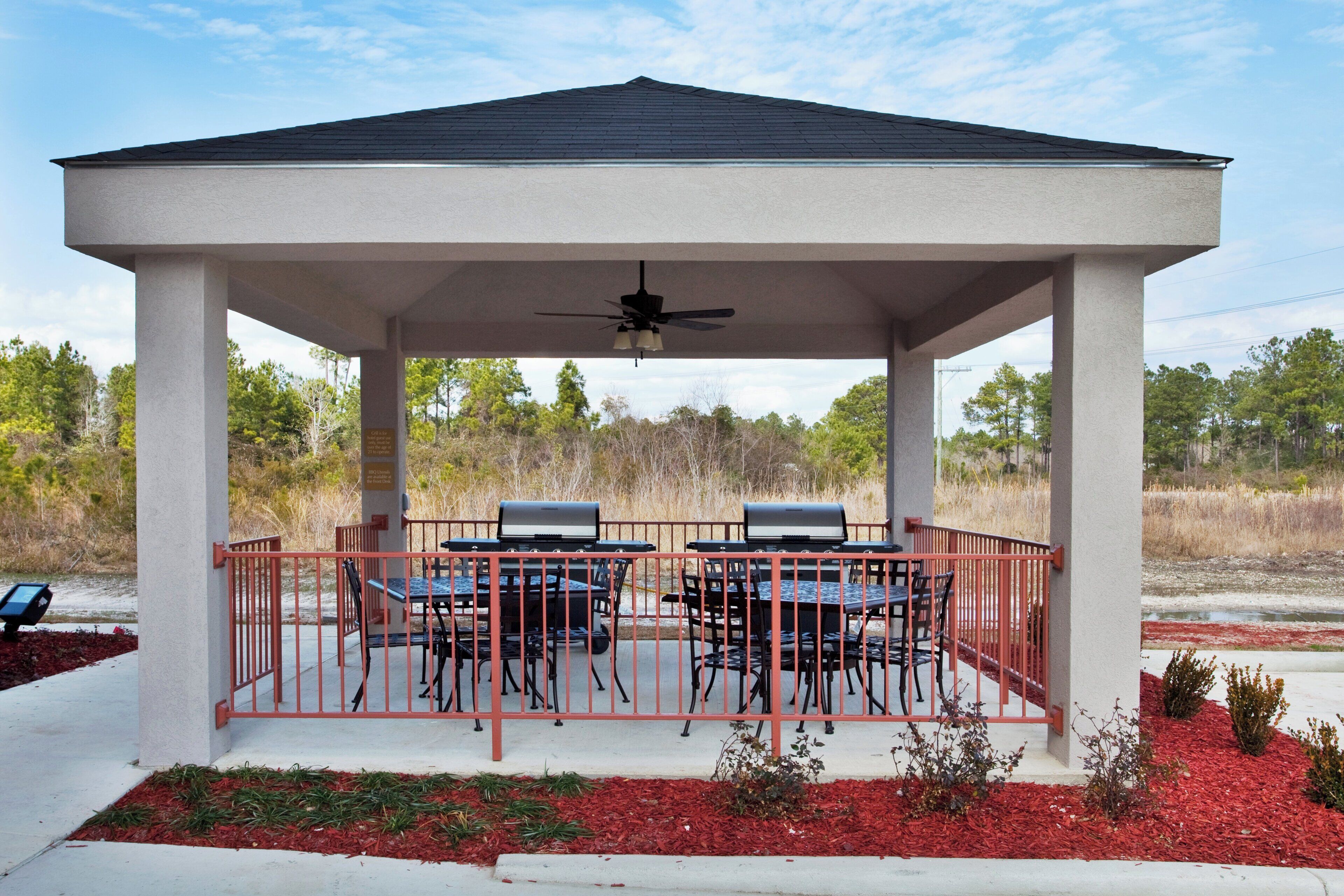 A covered pavilion with a table and chairs, a ceiling fan, and a grill.