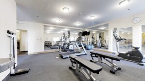 Een sportschool met loopbanden, elliptische trainers en een bank.
