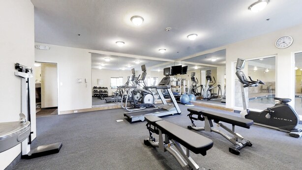A gym with treadmills, elliptical machines, and a bench.
