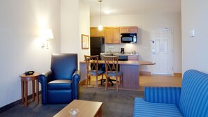 Een compacte leefruimte met een kitchenette, een blauwe bank, een zithoek met stoelen en een kleine tafel.