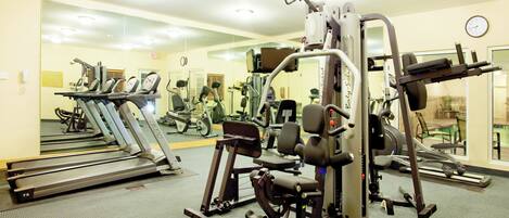 Un gimnasio con cintas de correr, máquinas de pesas y un muro de espejos.