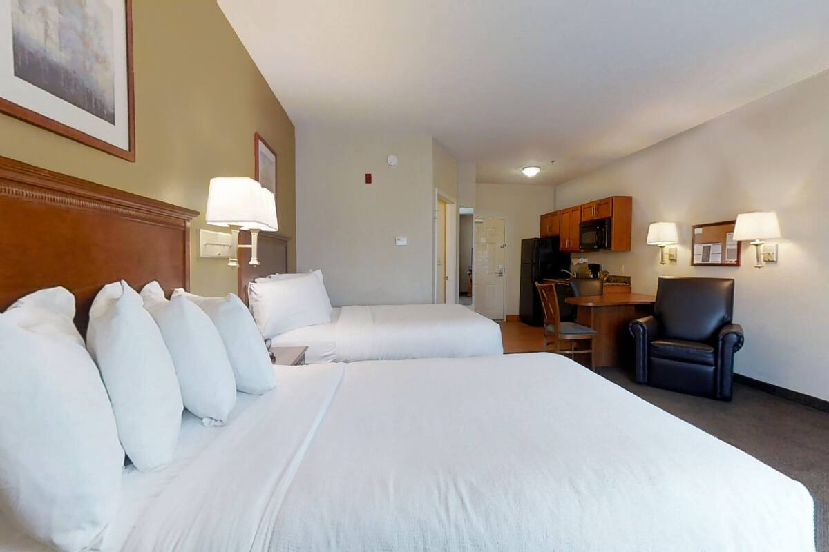 Une chambre d’hôtel avec deux lits, un bureau, une chaise et une kitchenette.