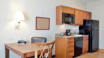 A compact kitchen with wooden cabinets, a microwave, a refrigerator, a coffee maker, and a telephone.