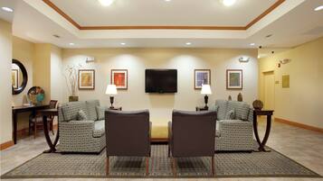 Une chambre d’hôtel comprenant deux fauteuils, un canapé, un téléviseur à écran plat fixé au mur et une table à manger avec des chaises.
