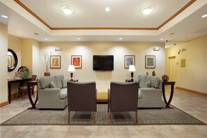 A hotel room with two armchairs, a sofa, a flat-screen TV mounted on the wall, and a dining table with chairs.