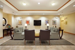 Habitación de hotel con dos sillones, un sofá, un televisor de pantalla plana en la pared y una mesa de comedor con sillas.