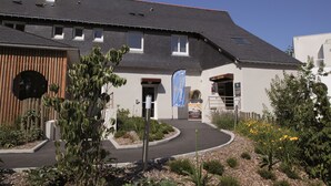 Ein modernes Gebäude mit Pultdach, Holzfassade und einer begrünten Eingangspforte mit Pflanzen und Blumen.