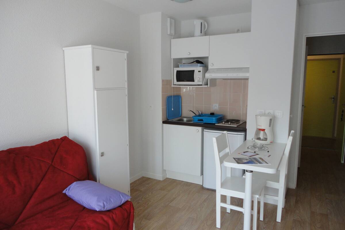 Una cocina compacta con armarios blancos, microondas, cafetera y una pequeña mesa de comedor con sillas.