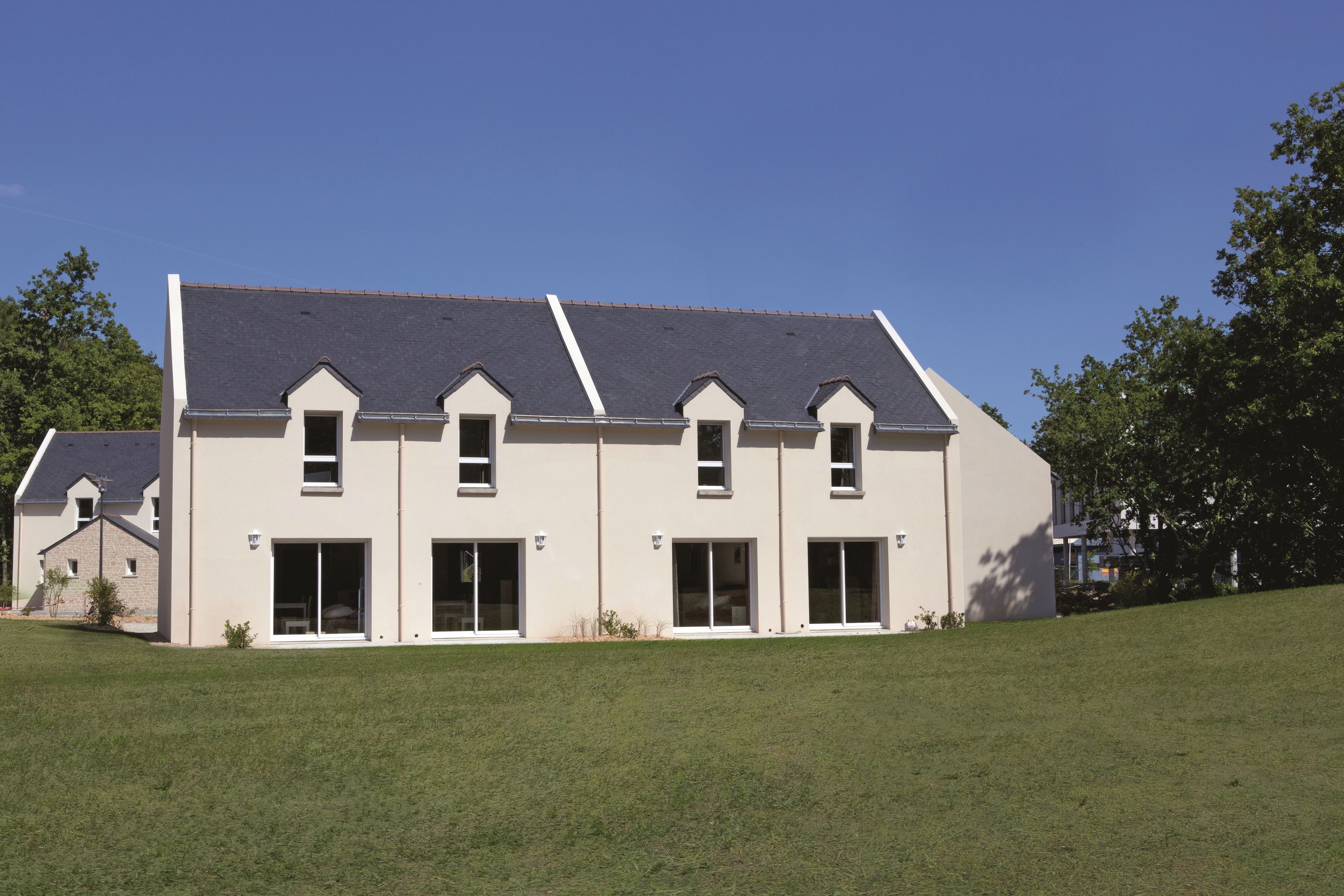 A modern two-story house with a sloped roof, large windows, and a grassy front yard.