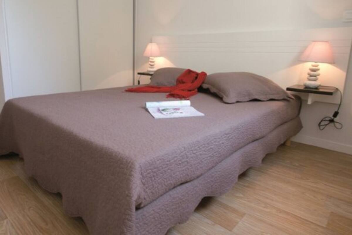 Una cama bien hecha con una cubierta marrón, dos lámparas de noche y un objeto rojo sobre la cama.