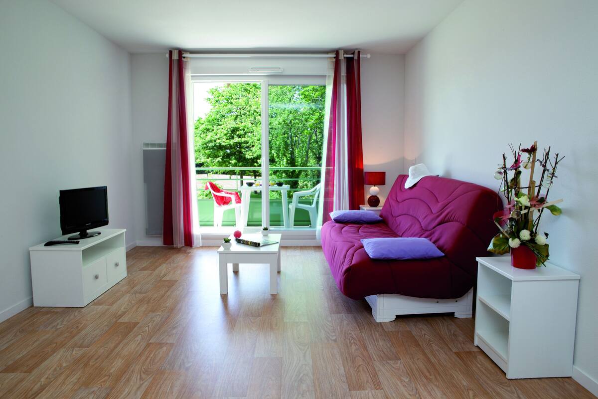 Un salón moderno con sofá, mesa de centro, televisor y balcón con vistas a zonas verdes.