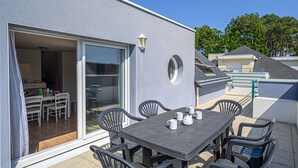 Eine Terrasse mit Tisch und Stühlen, eine Schiebetür zu einem Innenbereich und ein kleines rundes Fenster in der Außenwand.