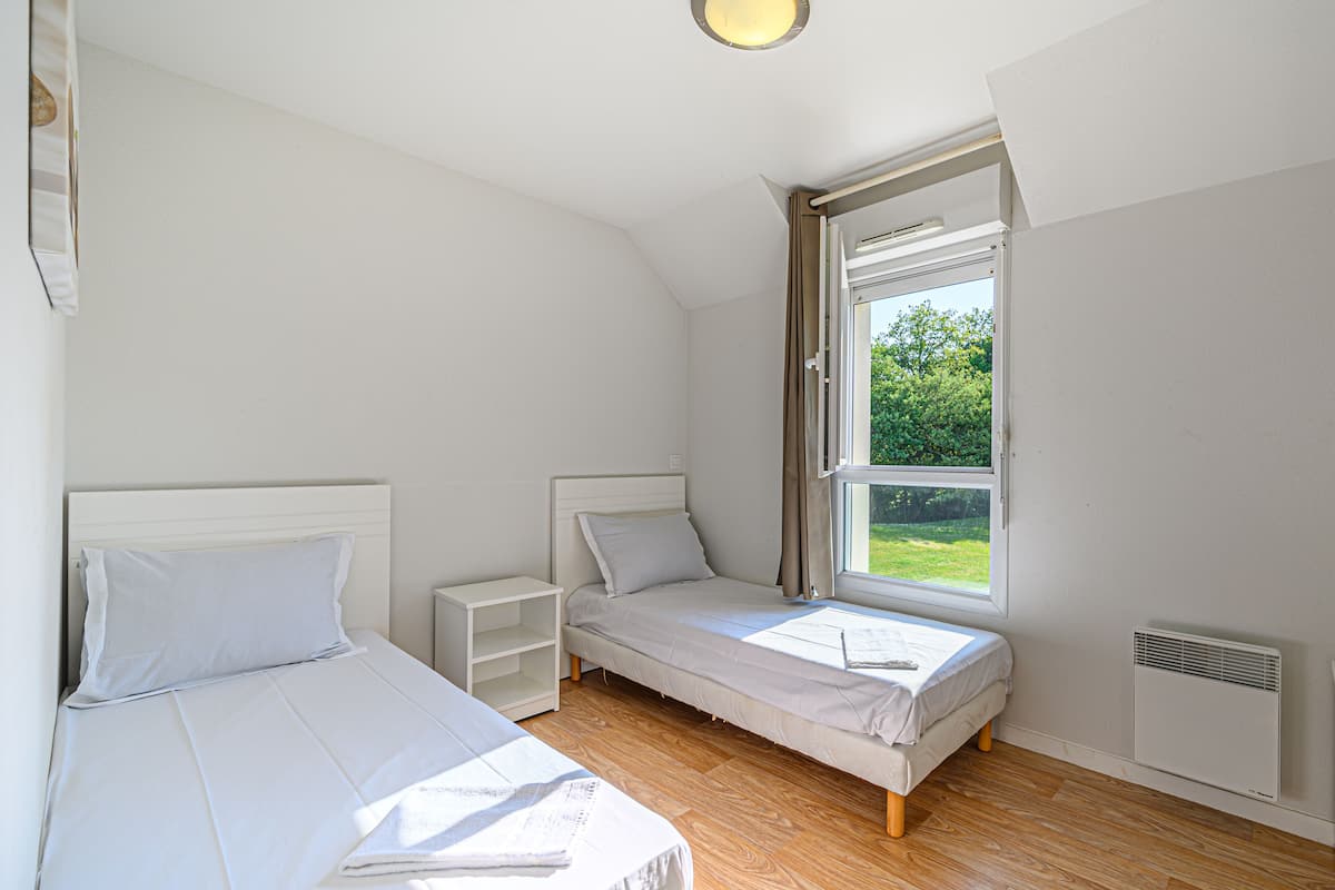 Un dormitorio con dos camas, una ventana, una mesita de noche y un radiador.