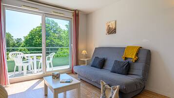 A living room with a grey sofa, a white coffee table, and a balcony with white chairs.