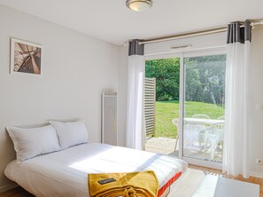 Relax in a serene space with a large bed, framed artwork, and a patio area offering a garden view.