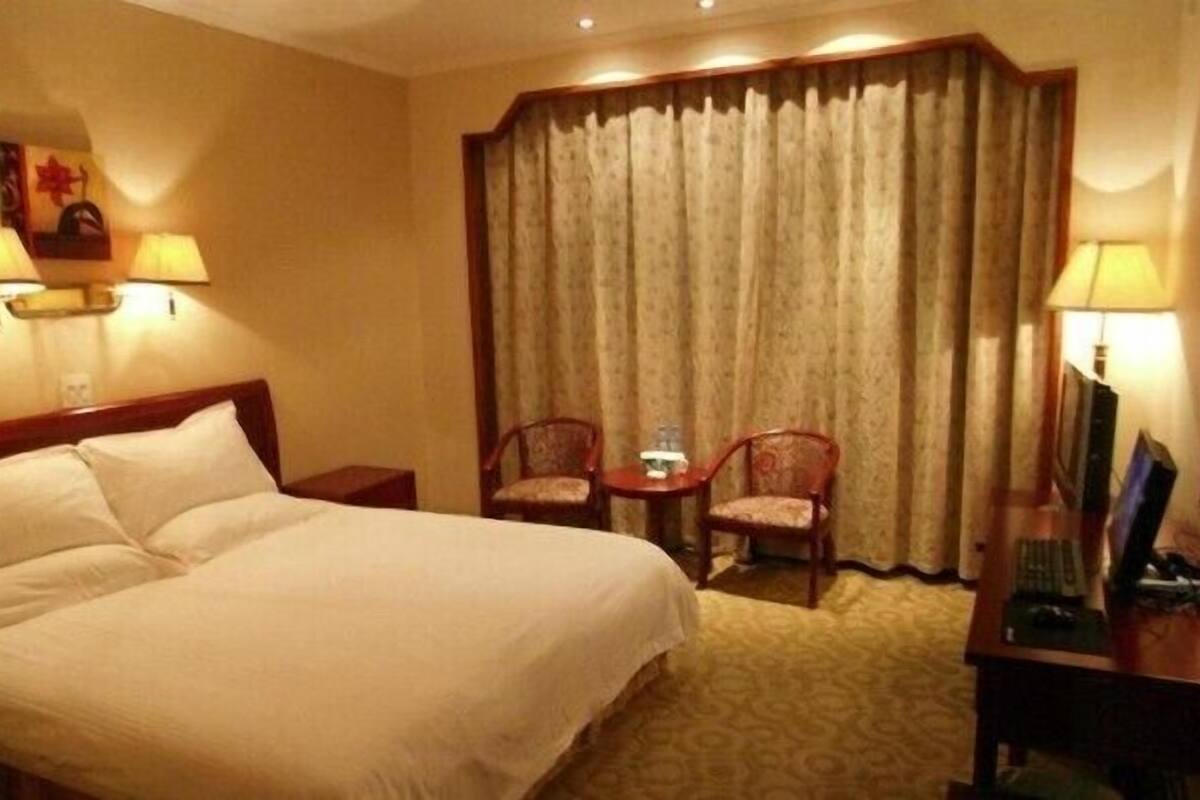 Une chambre d’hôtel avec un grand lit, deux chaises, une petite table et un bureau avec un ordinateur.