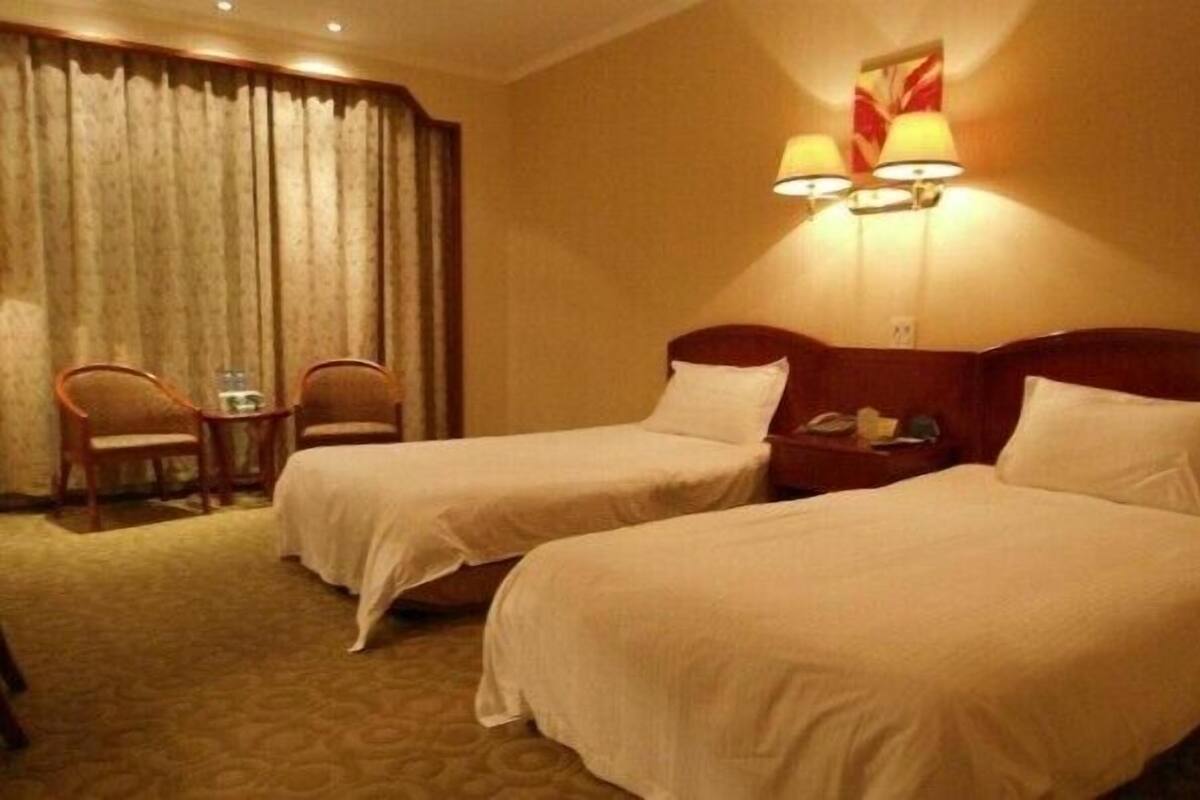 Une chambre d’hôtel avec deux lits simples, une petite table avec des chaises et une lampe fixée au mur.