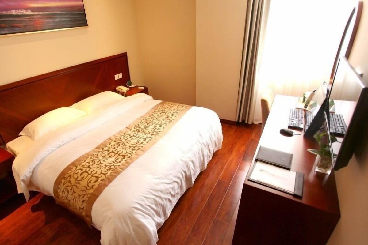 Une chambre d’hôtel avec un grand lit, un bureau avec un ordinateur et un tableau au mur.