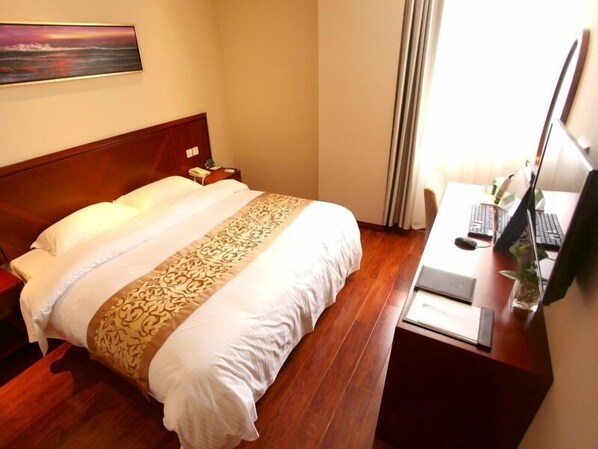 Una habitación de hotel con una cama grande, un escritorio con una computadora y un cuadro en la pared.
