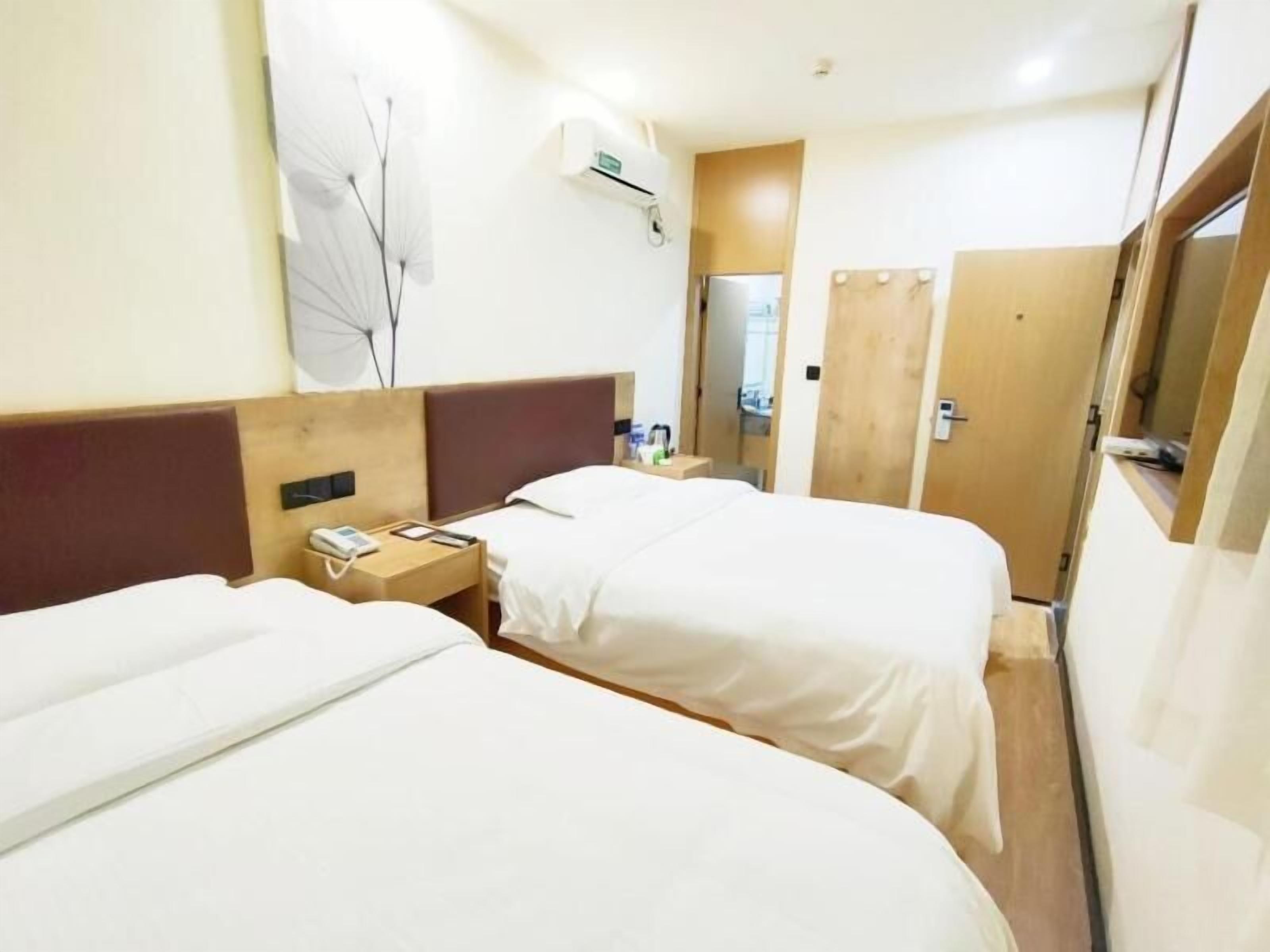 A hotel room with two beds, a bedside table with a phone, and a wall-mounted air conditioner.