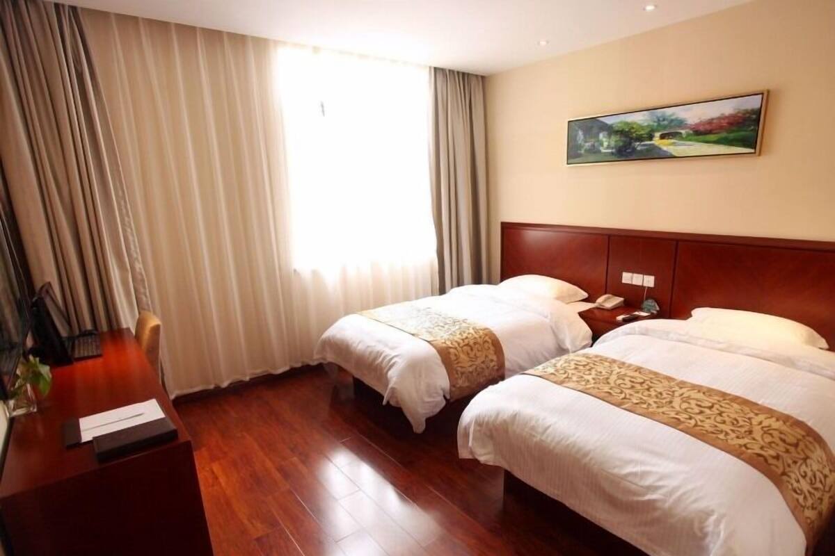 Une chambre d’hôtel avec deux lits, un bureau en bois, un tableau au mur et une fenêtre avec des rideaux.