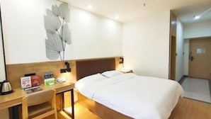 Une chambre d’hôtel équipée d’un lit, d’un bureau, d’une chaise, d’une table de chevet et d’une lampe fixée au mur.