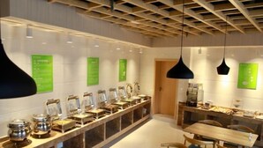 A modern cafe with a long counter, multiple food dispensers, wooden tables, and chairs. - GreenTree Inn Wuxi ChongAn Temple Jiefang West Road Hotel (Wuxi)