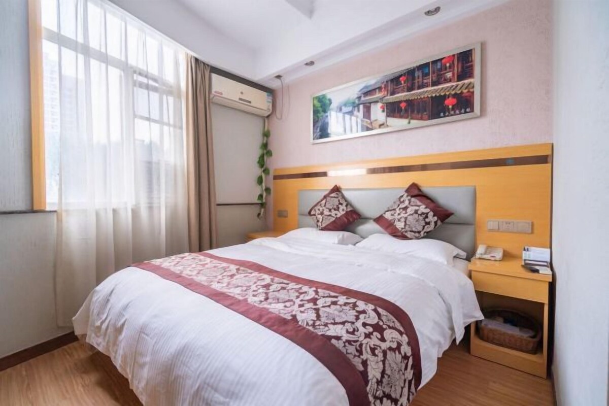A hotel room with a large bed, a bedside table with a phone, and a window with curtains.