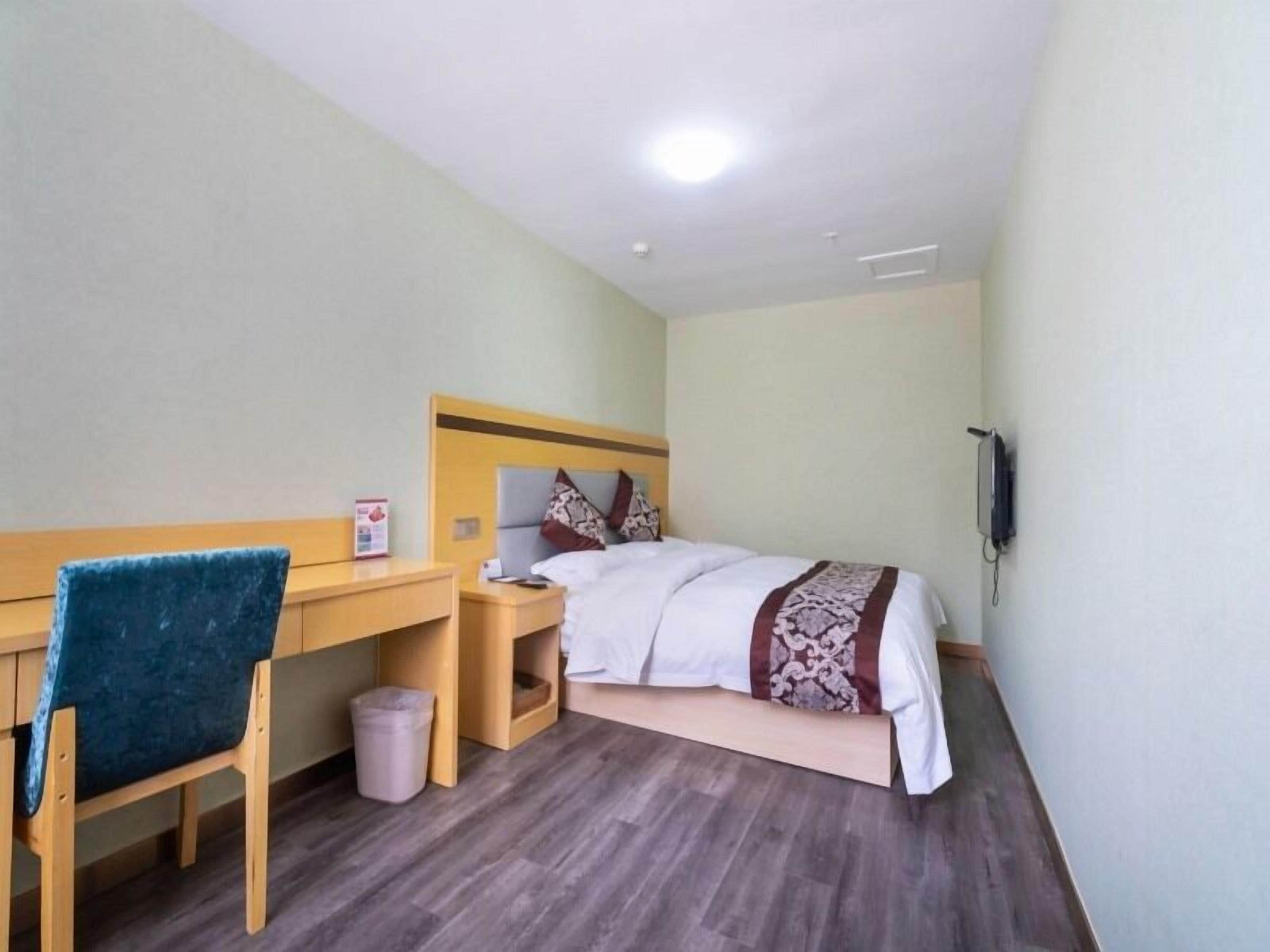 A hotel room with a bed, a desk, a chair, a trash bin, and a wall-mounted phone.