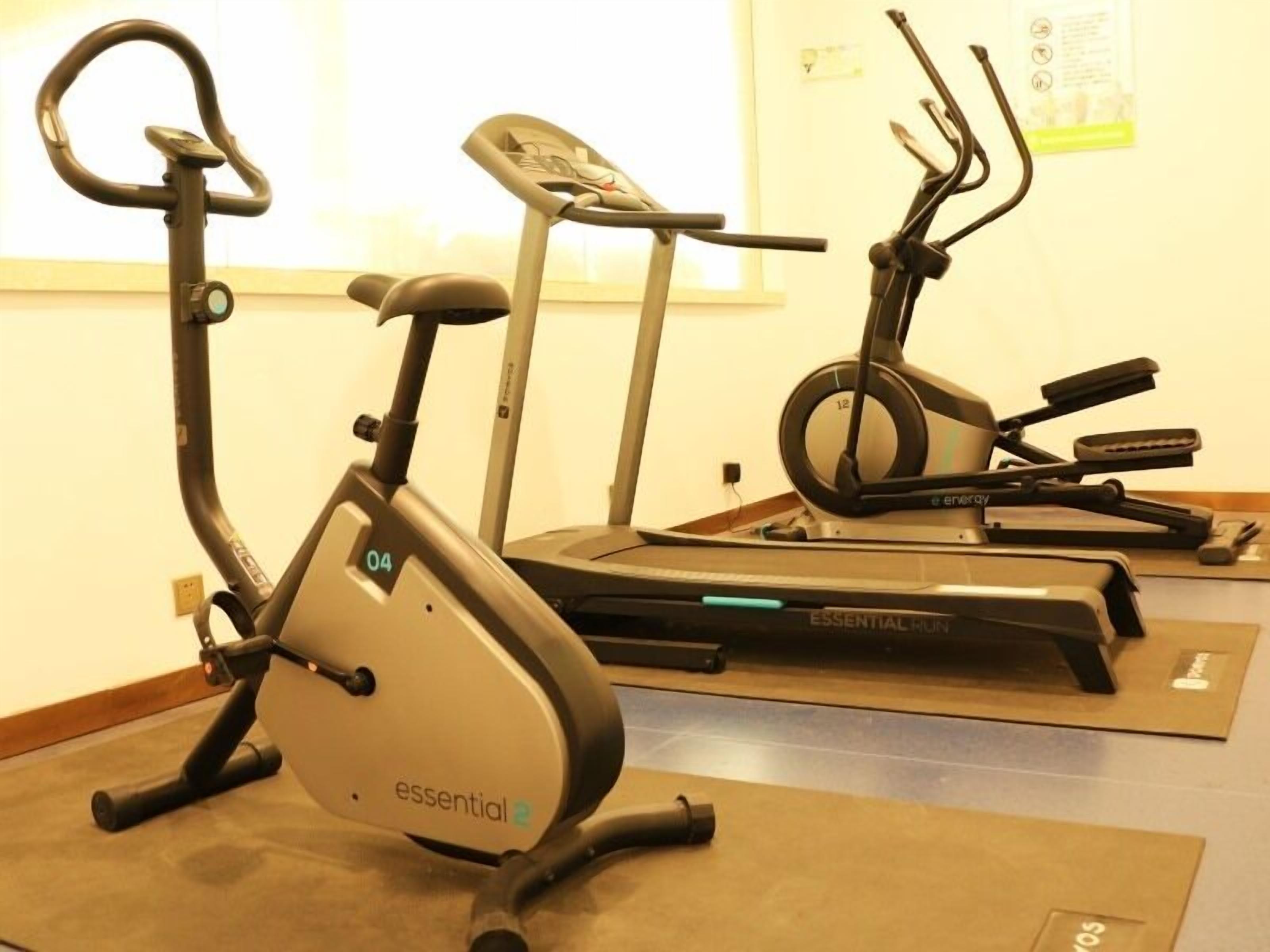 Three stationary bikes in a gym with a plain wall and a window in the background.
