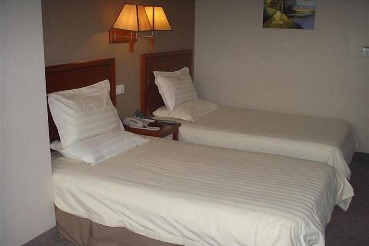 Zwei Betten mit weißer Bettwäsche in einem Hotelzimmer.