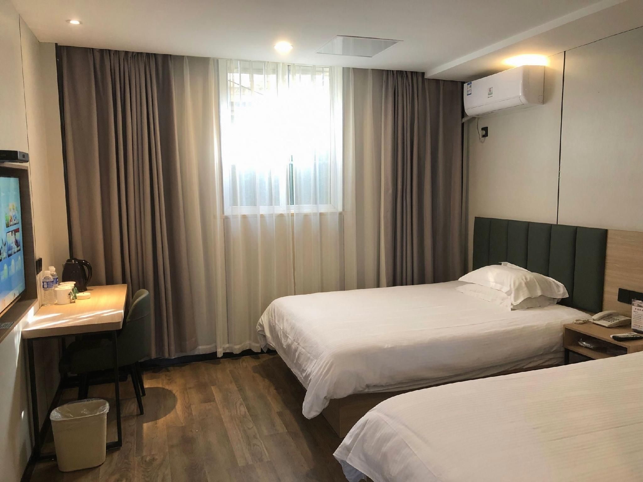 A hotel room with two beds, a desk with a chair, a TV, and a window with curtains.