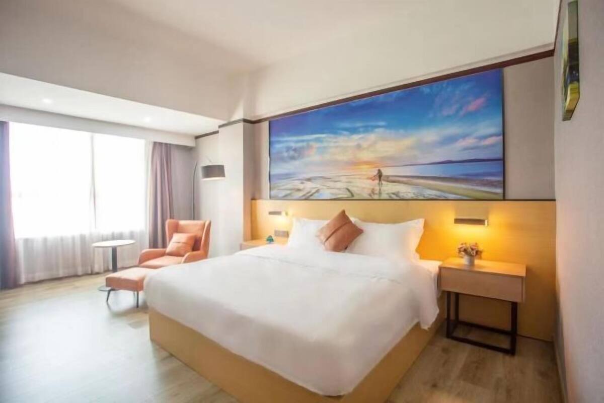Relax in comfort with a large bed, a wall-mounted lamp, and a scenic painting above.