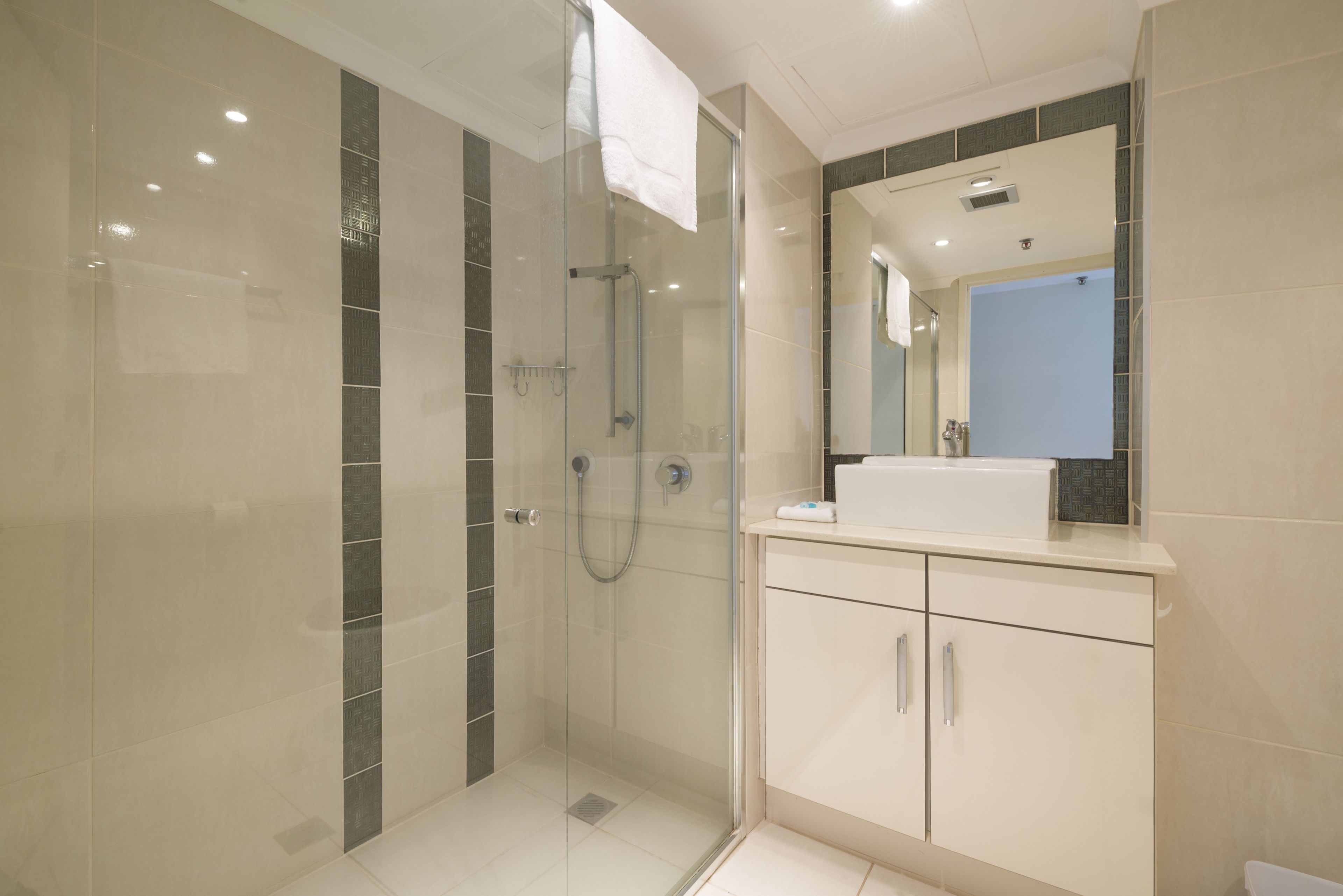 A modern bathroom with a glass-enclosed shower, a white sink, and a large mirror above the vanity.