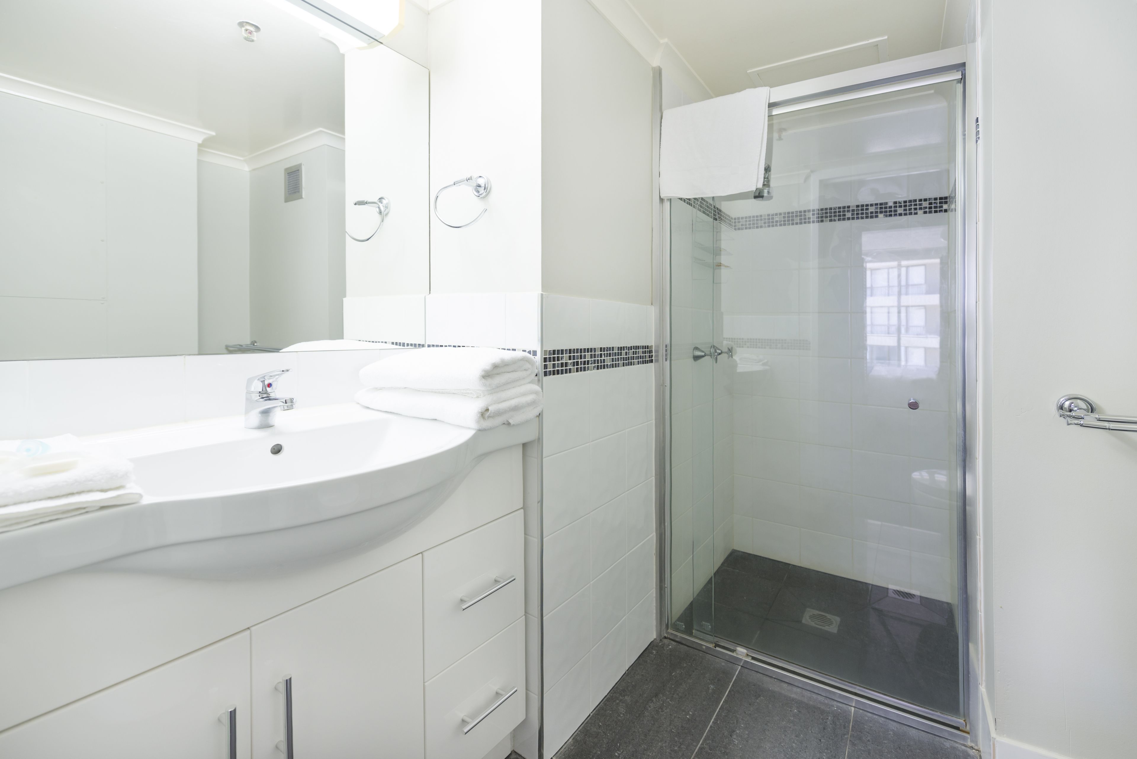Un baño con lavamanos blanco, espejo y cabina de ducha de vidrio.