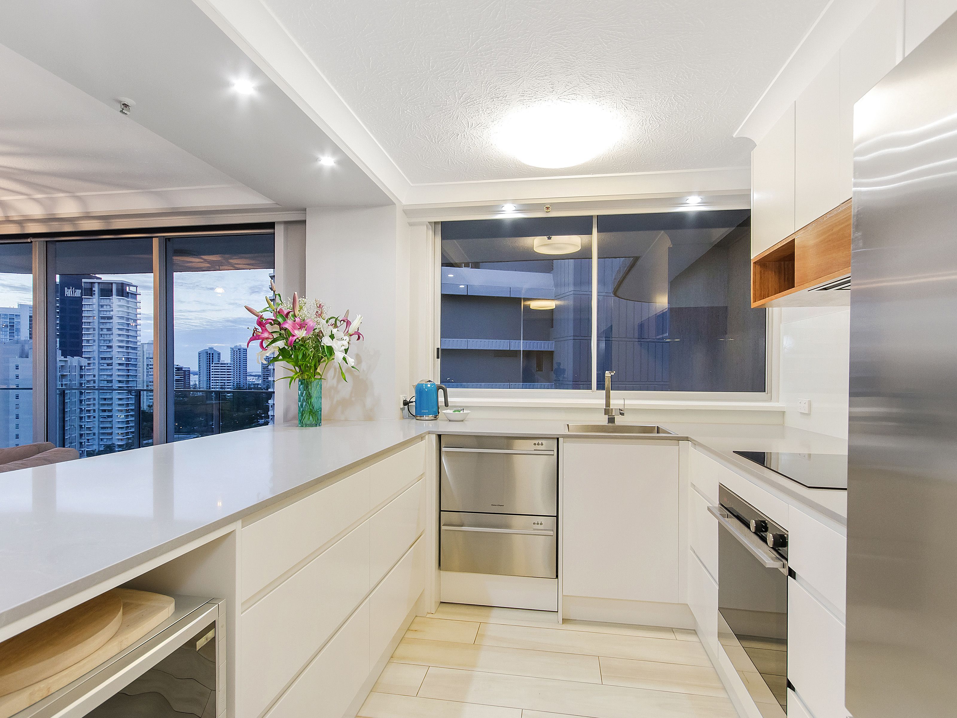 A modern kitchen with a view of the cityscape, stainless steel appliances, and a vase of flowers on the counter.