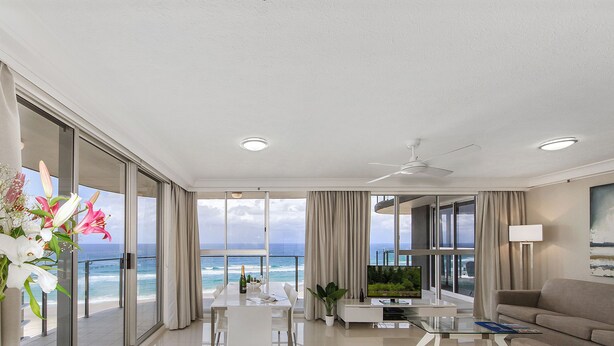 A modern hotel room with a balcony overlooking the ocean, a dining area, and a living space with a flat-screen TV. - Sunbird Beach Resort (Main Beach)