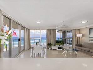 A modern hotel room with a balcony overlooking the ocean, a dining area, and a living space with a flat-screen TV. - Sunbird Beach Resort (Main Beach)