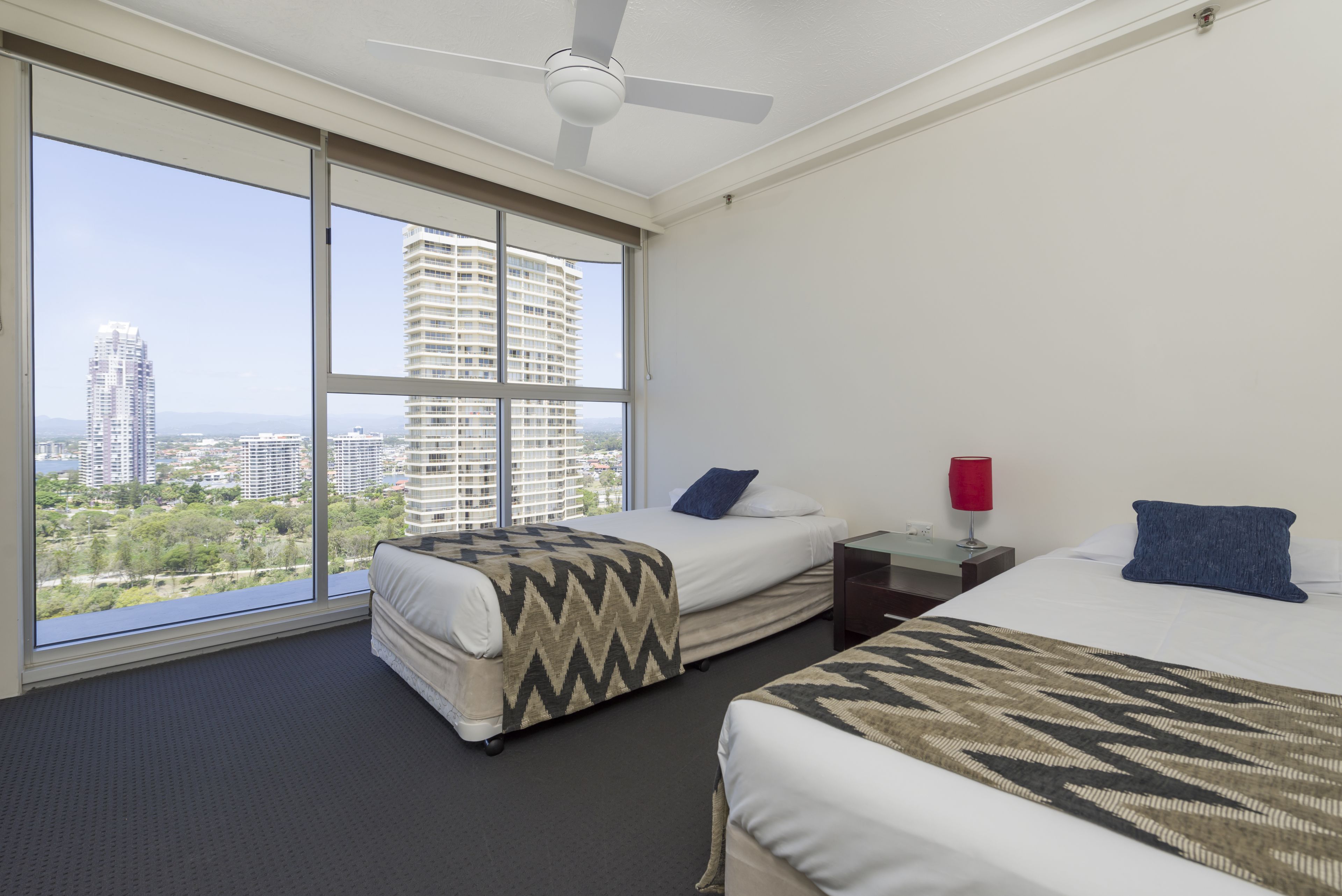 Habitación de hotel con dos camas, ventanas amplias, ventilador de techo y vista panorámica de la ciudad.