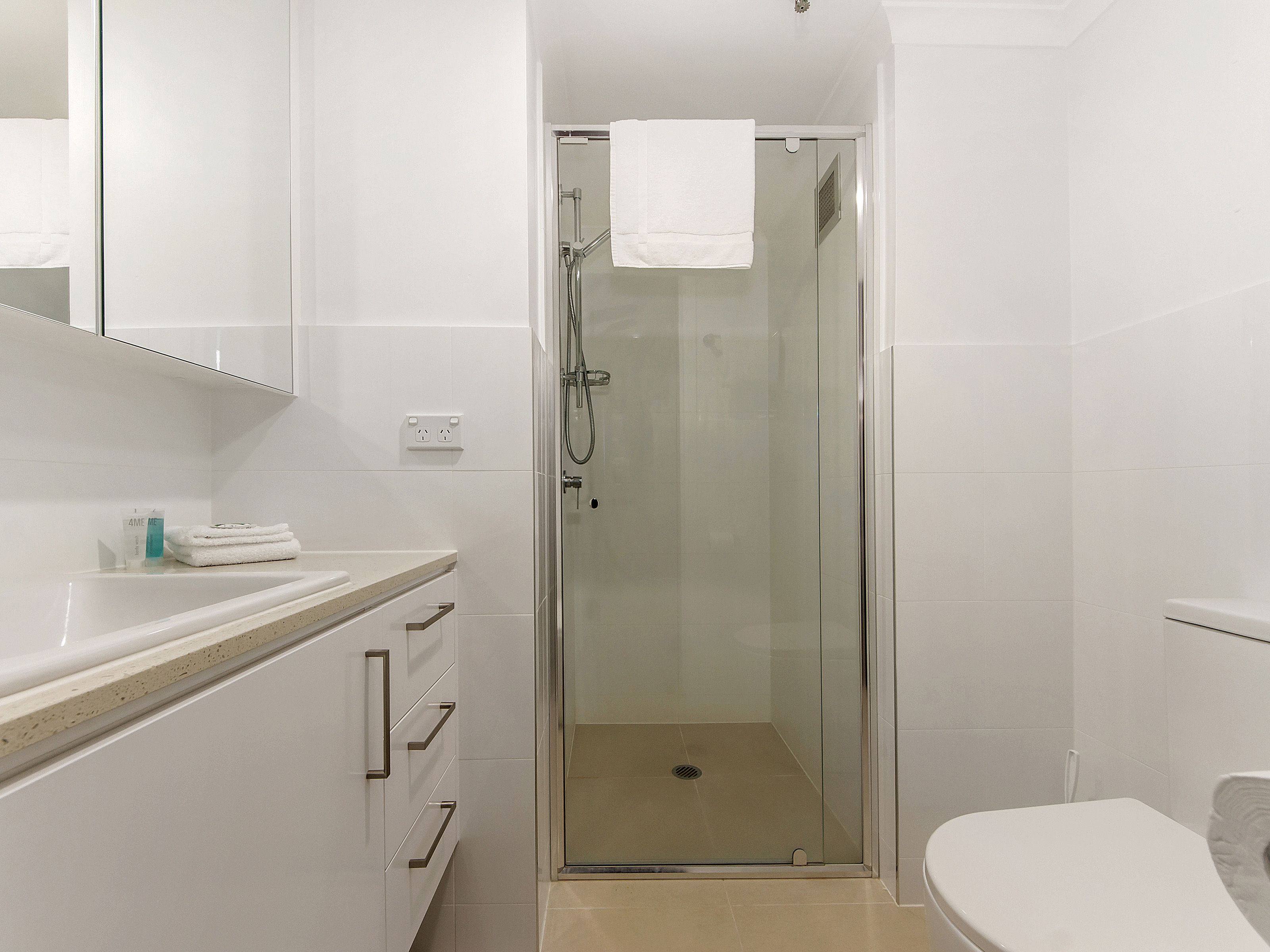 A modern bathroom with a glass-enclosed shower, a white toilet, and a vanity with a mirror and countertop.