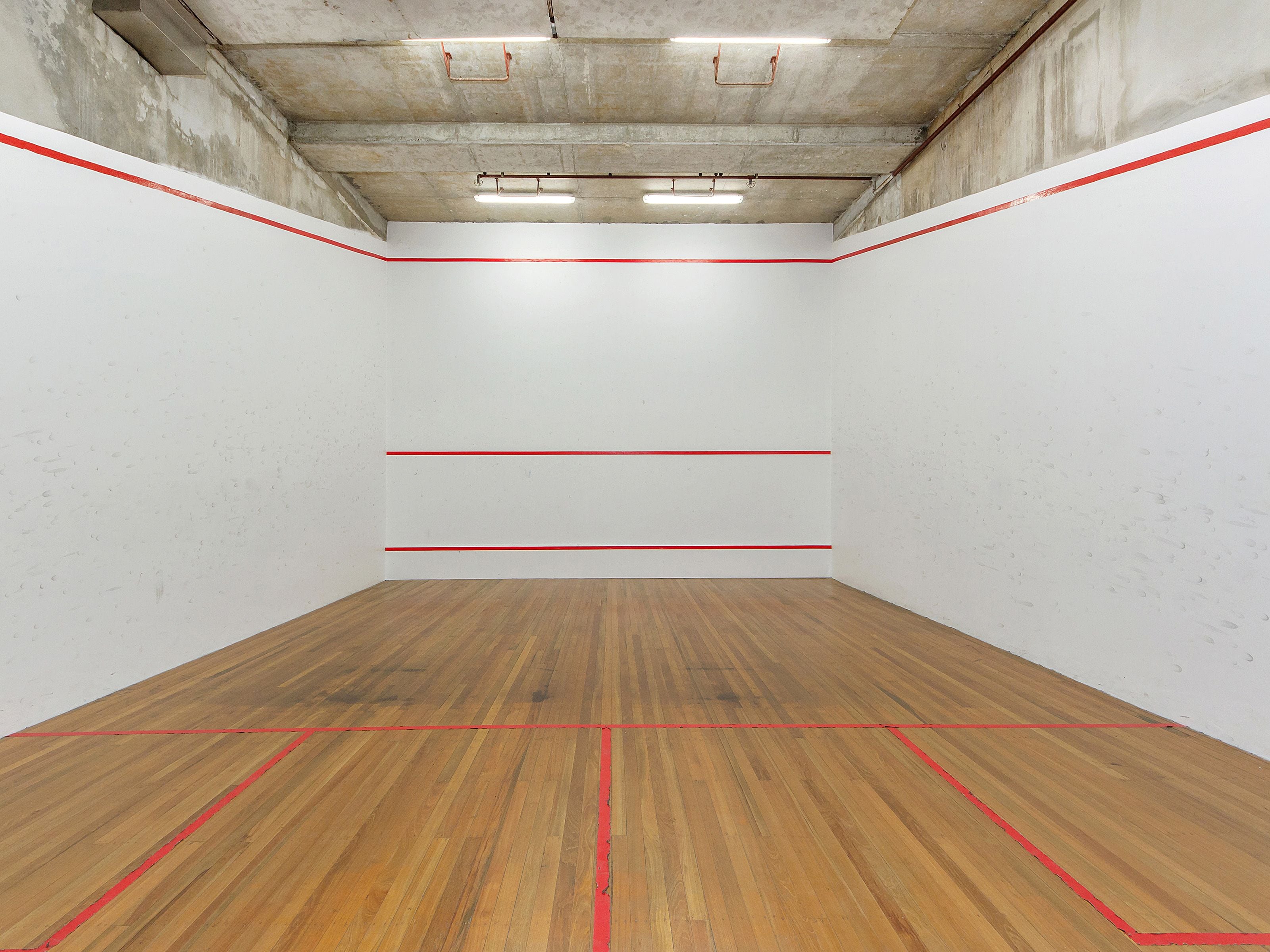 A squash court with wooden flooring and red lines marking the playing area.