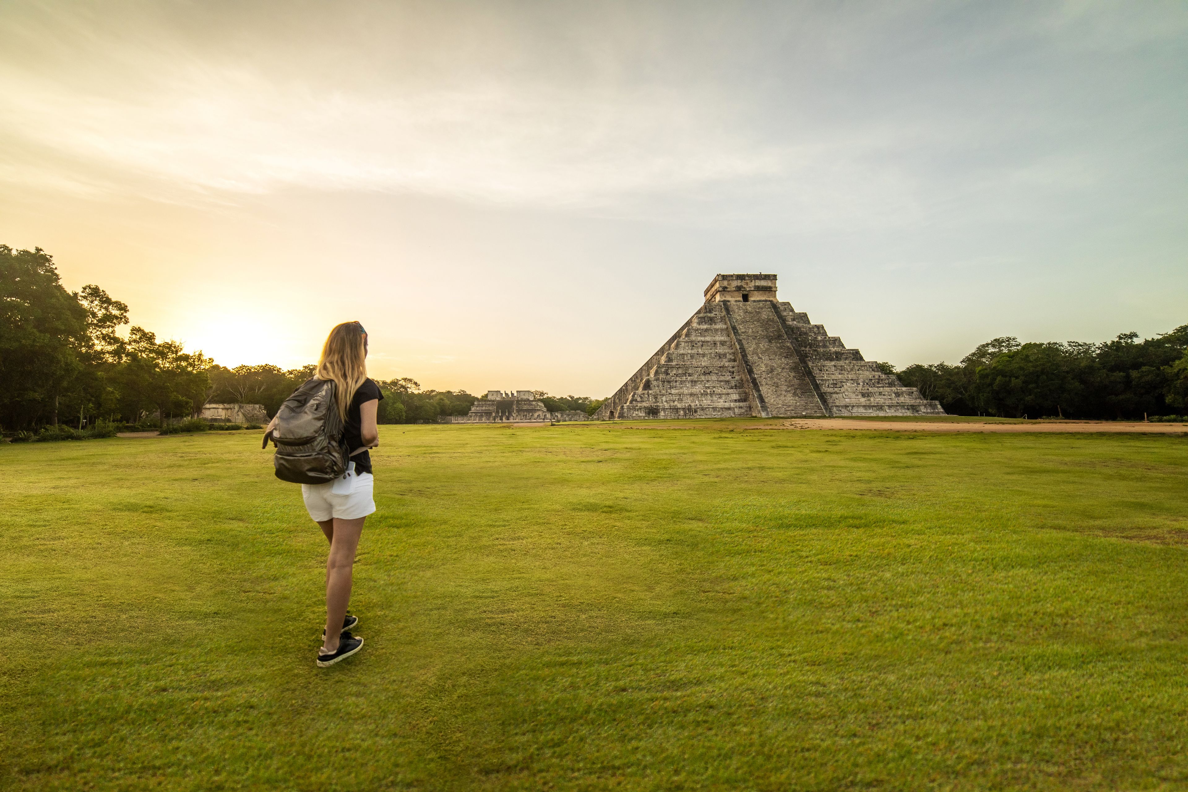 A person standing in a grassy field with a pyramid in the background.