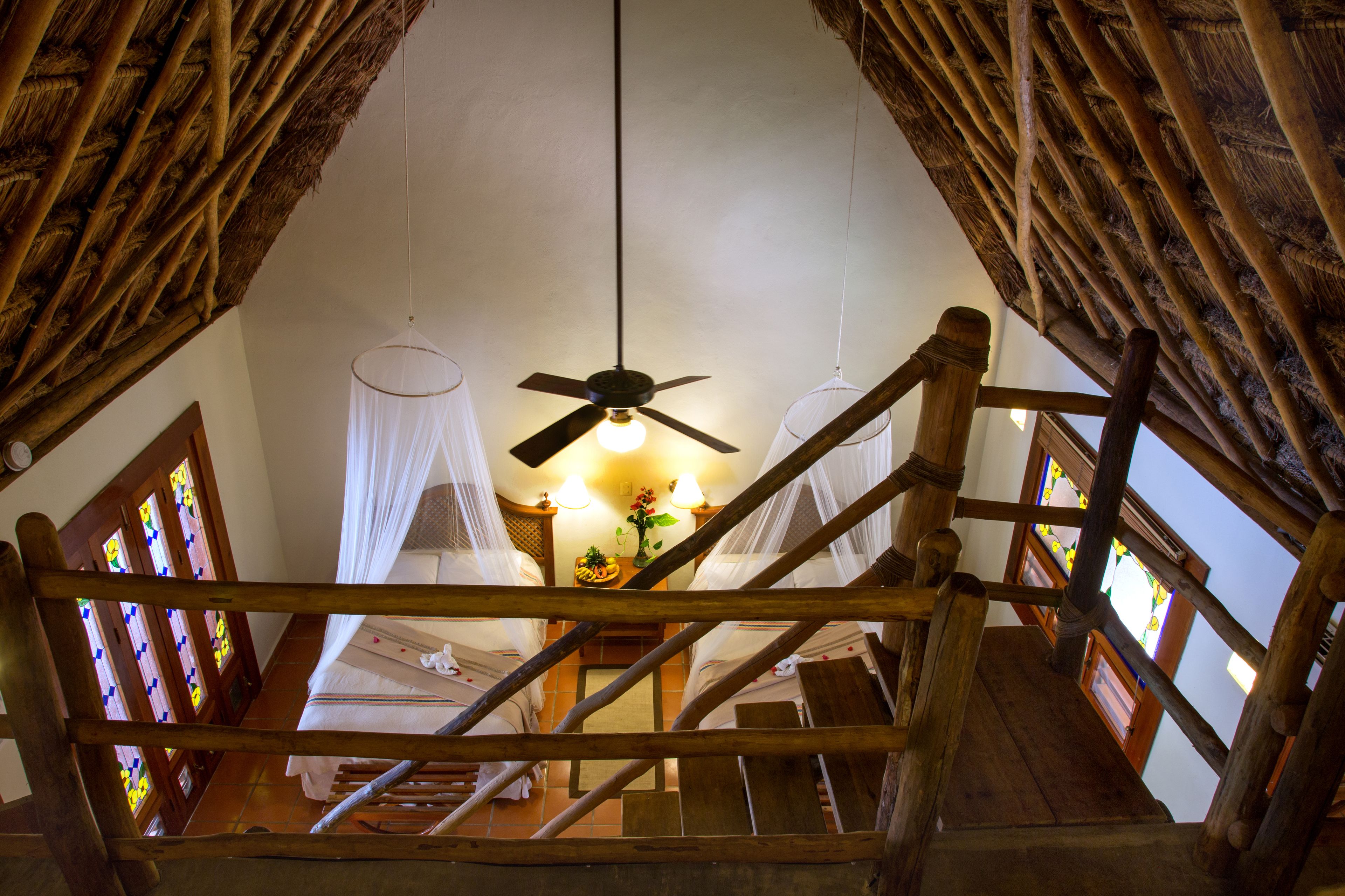 A wooden staircase leading to a room with a ceiling fan and a bed with white bedding.