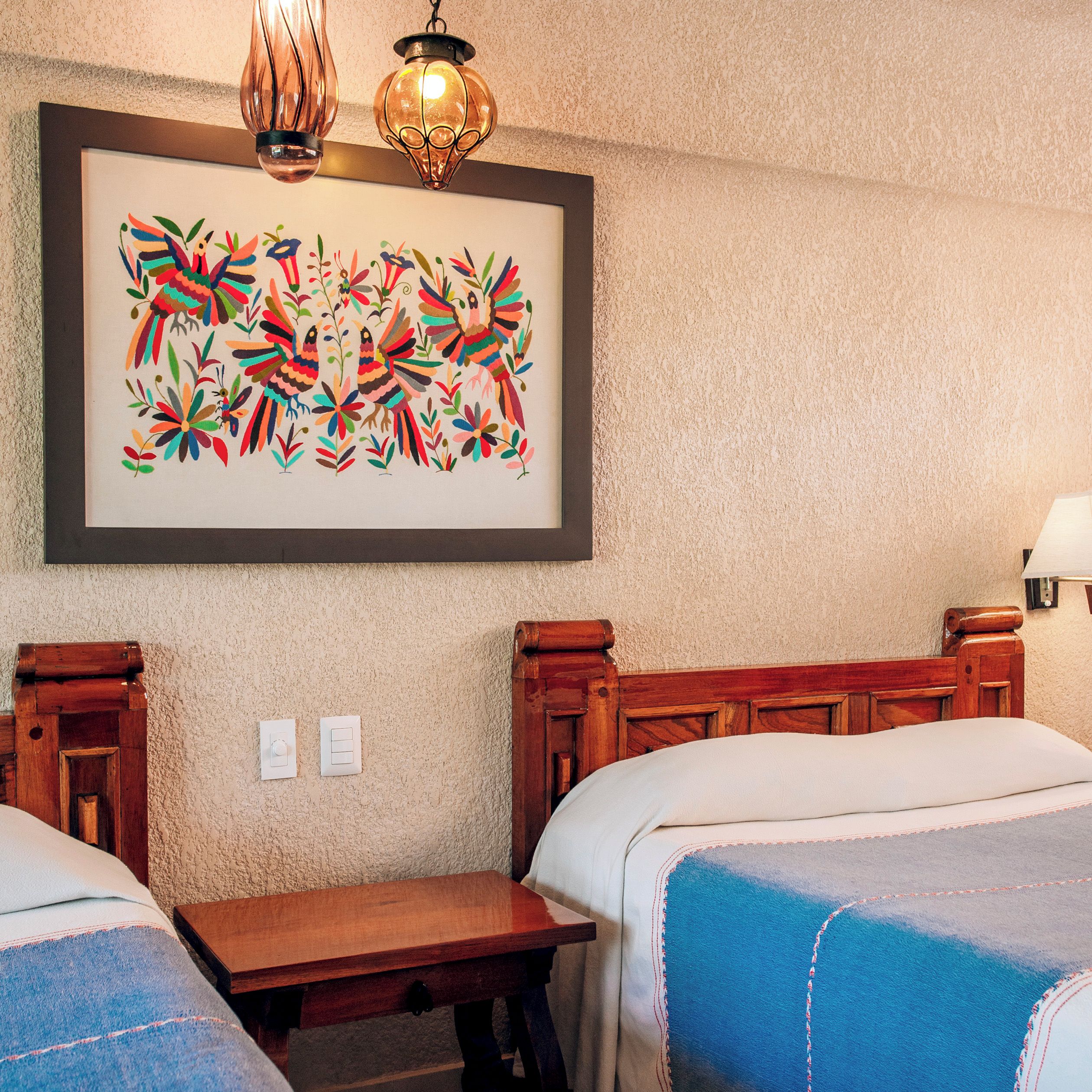 A hotel room with two beds, a wooden nightstand, a framed artwork, and a wall-mounted light fixture.