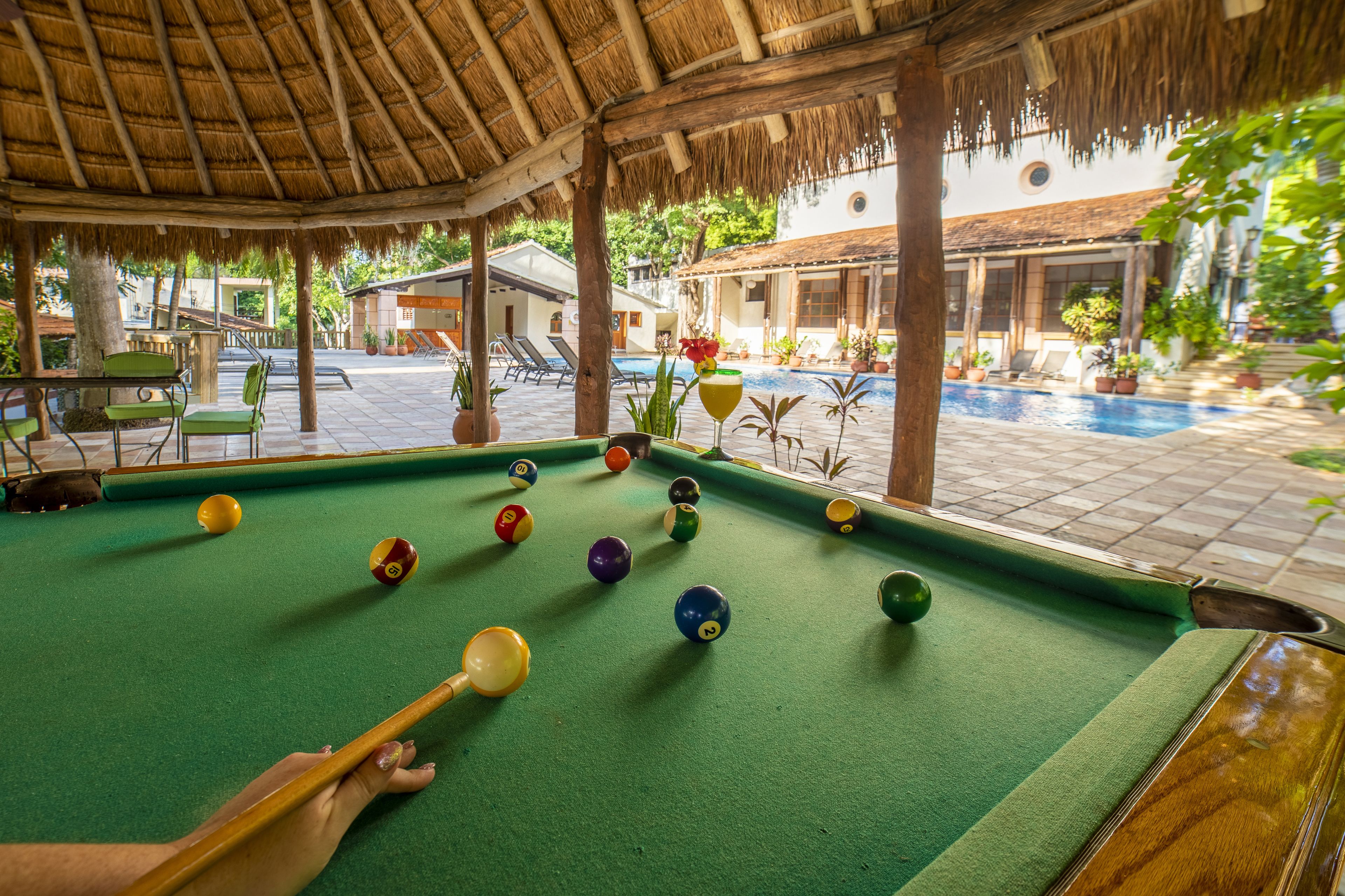 Une table de billard avec des billes, une queue de billard et une structure dotée d’un toit de chaume.