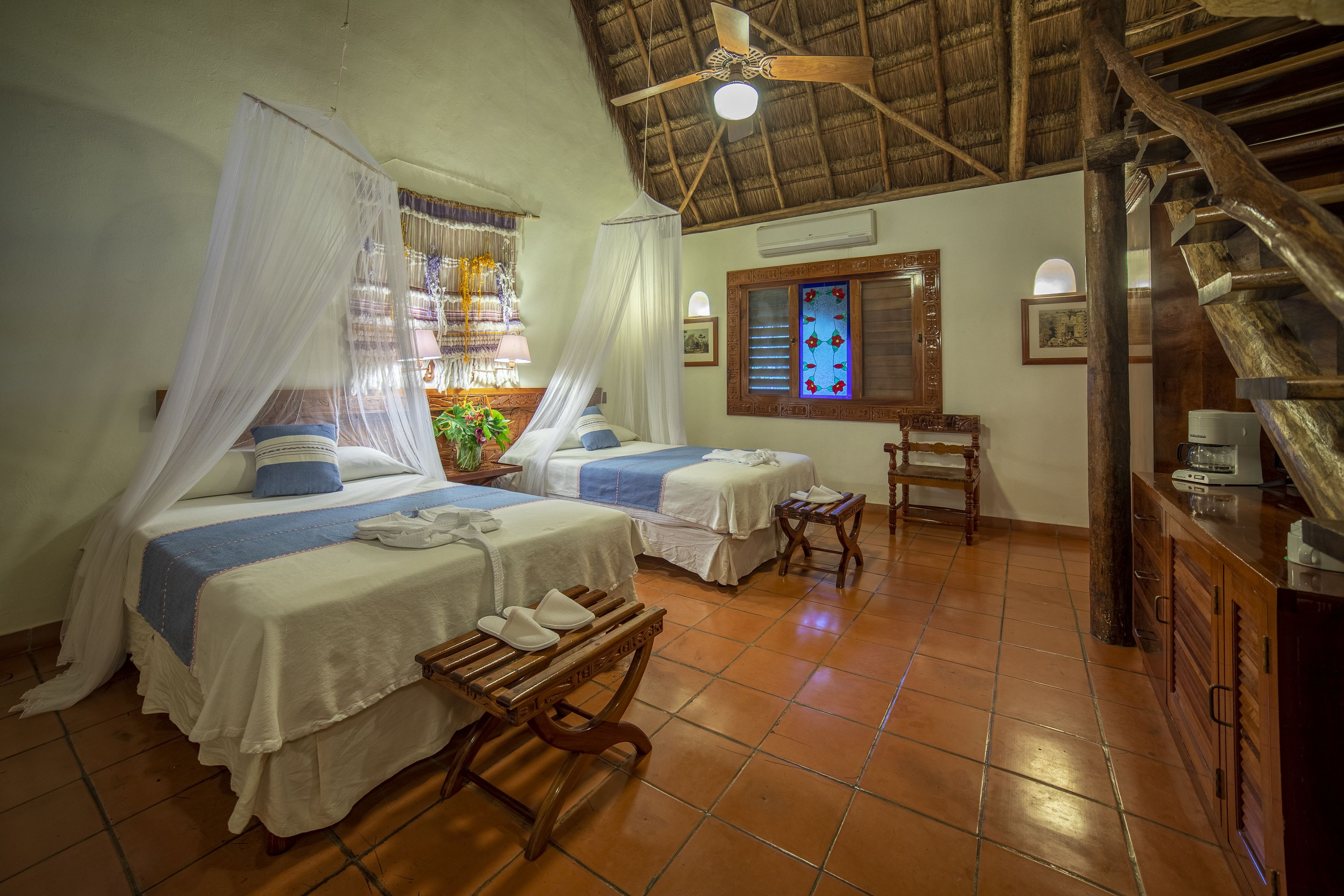 Una habitación con dos camas, un banco de madera, un escritorio y una escalera.