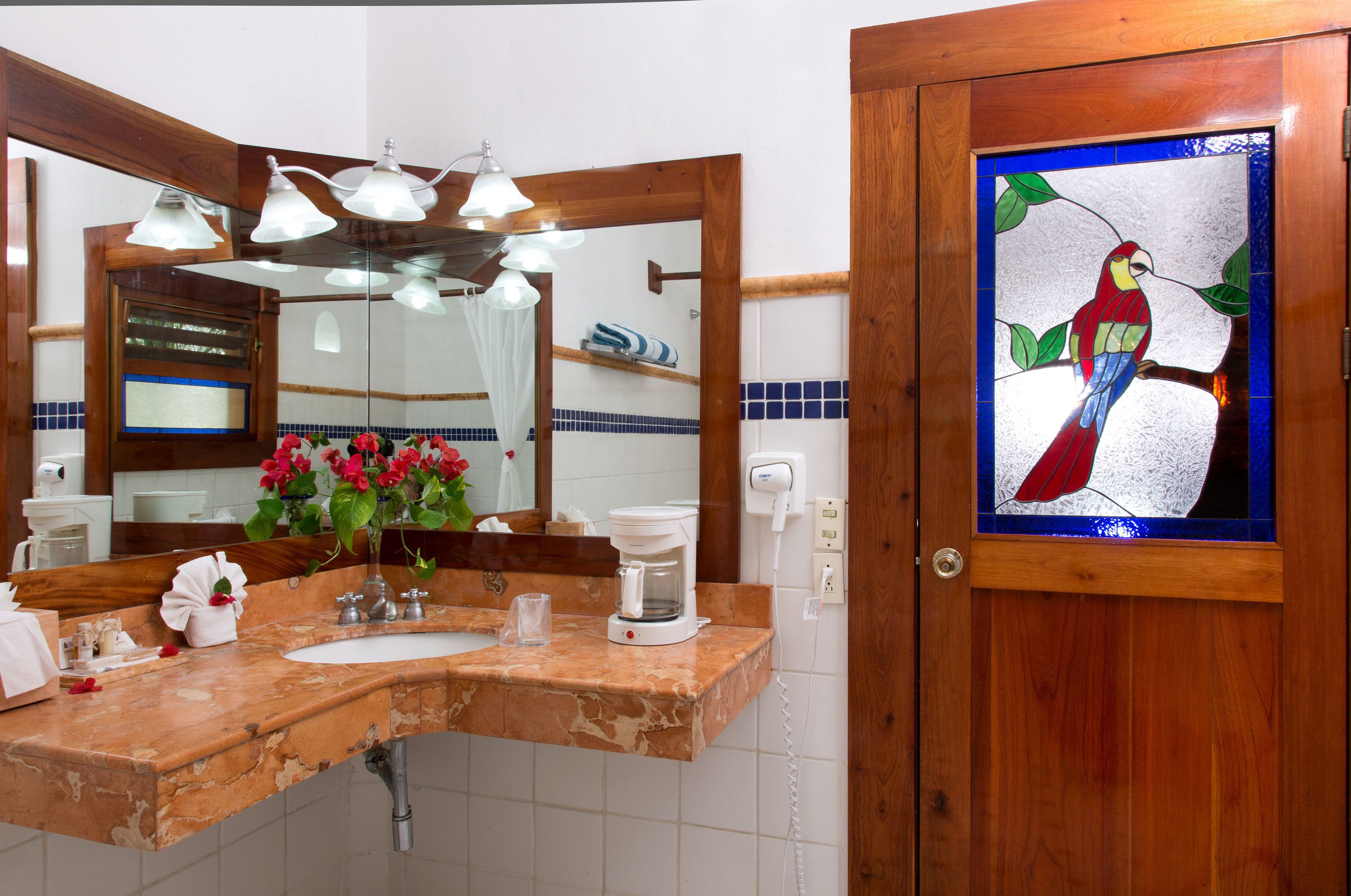 A bathroom with a wooden vanity, a mirror, a coffee maker, and a stained glass window depicting a bird.