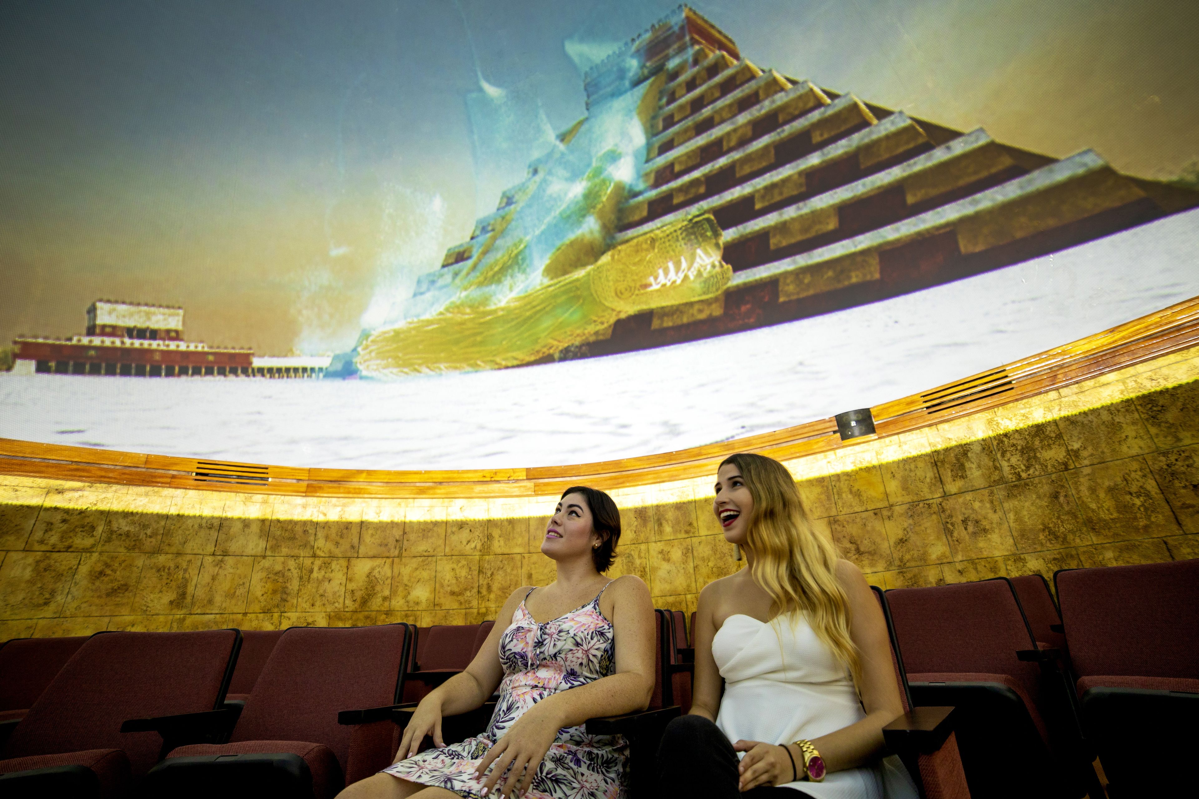 Un teatro interior con filas de asientos rojos y una gran pantalla mostrando un barco.