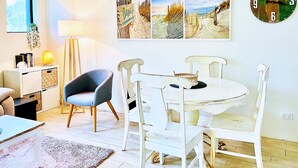Uma sala de jantar com uma mesa redonda branca e cadeiras, uma lâmpada e um relógio de parede.